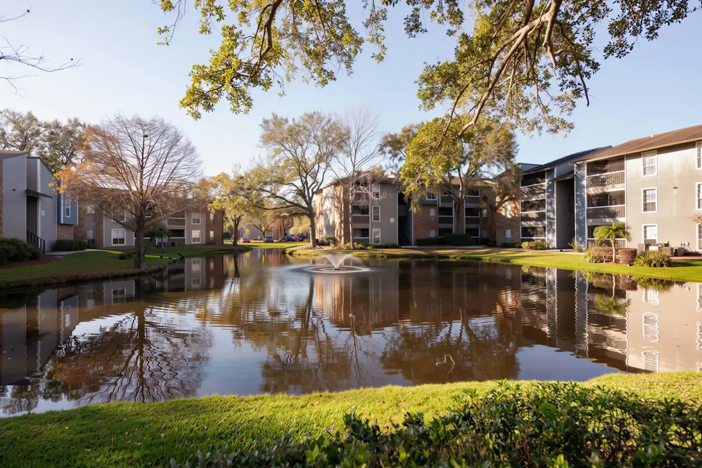 Scenic pond with fountain surrounded by Arbour Ponds apartment buildings and mature trees